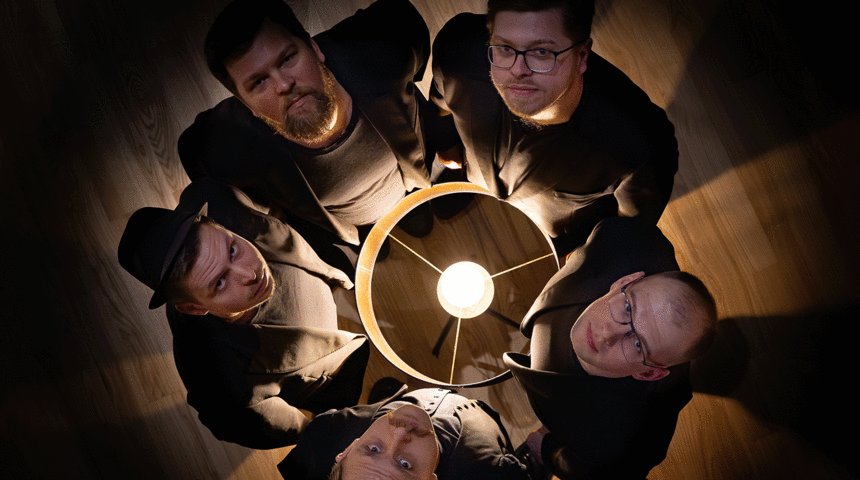 Die fünf Musiker der Band stehen im Kreis und sehen nach oben. Von oben fotografiert. In der Mitte eine Stehlampe.