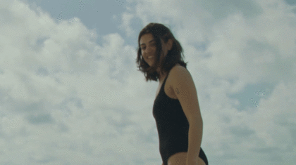 Eine lächelnde Frau im Badeanzug vor weiß-blauem Himmel.