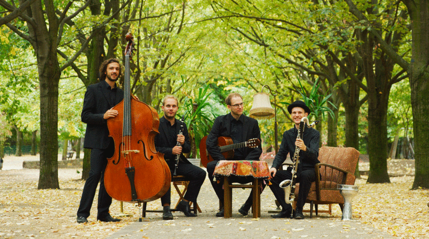 Bandfoto mit vier Musikern und Instrumenten in einem Park.