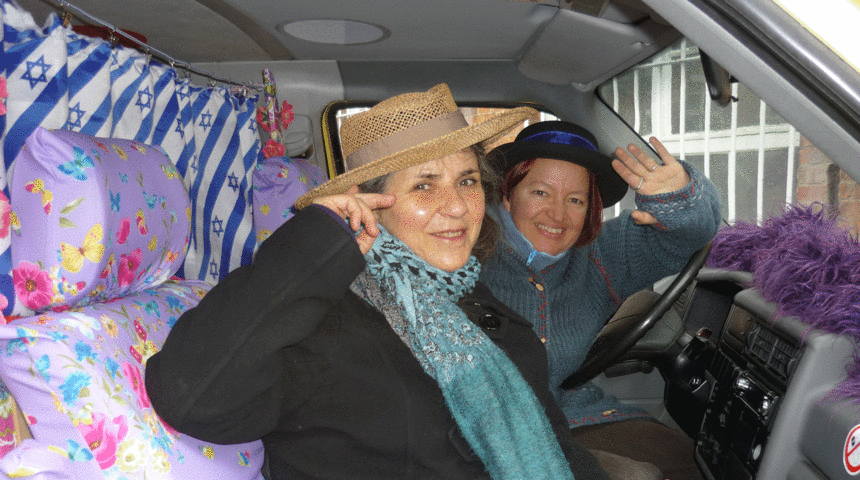 Zwei Frauen sitzen winkend in einem Bus.